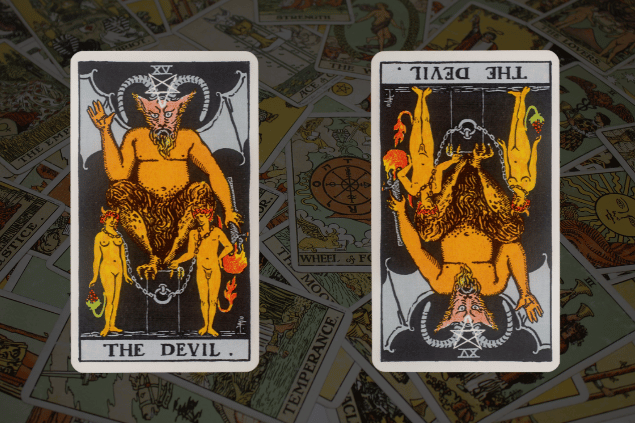 Montagem com a carta O Diabo do Tarot na posição normal e outra carta O Diabo na posição invertida. Ao fundo, há várias cartas de Tarot.
