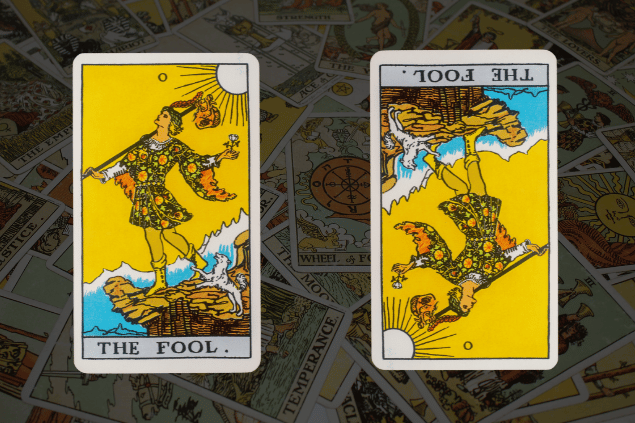 Montagem com a carta O Louco do Tarot na posição normal e outra carta O Louco na posição invertida. Ao fundo, há várias cartas de Tarot.