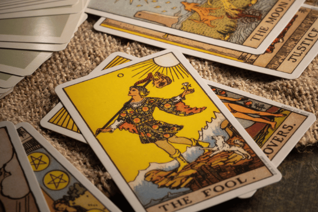 A carta O Louco do Tarot está em destaque sobre uma mesa. Ao lado, há outras cartas de Tarot.