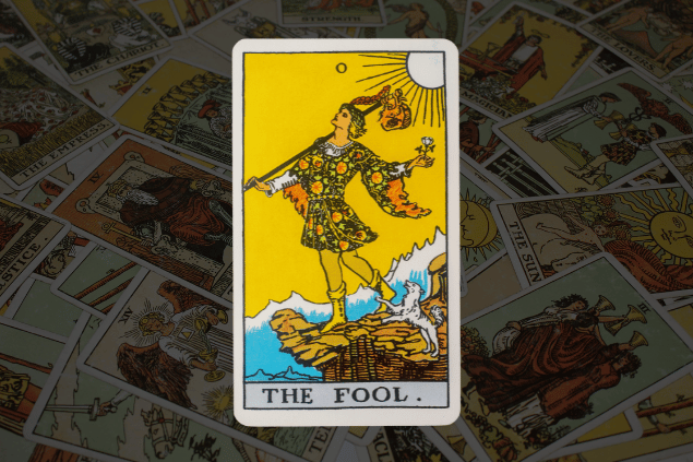 Montagem com a carta O Louco do Tarot na posição normal. Ao fundo, há várias cartas de Tarot.