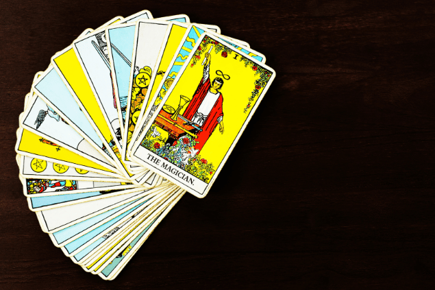 Várias cartas de Tarot estão espalhadas em sequência sobre uma mesa de madeira. A carta O Mago está destaque no final da sequência.