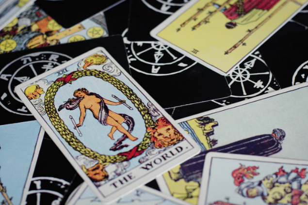 A carta O Mundo do Tarot está sobre uma mesa em destaque. Ao lado dela, há outras cartas espalhadas.