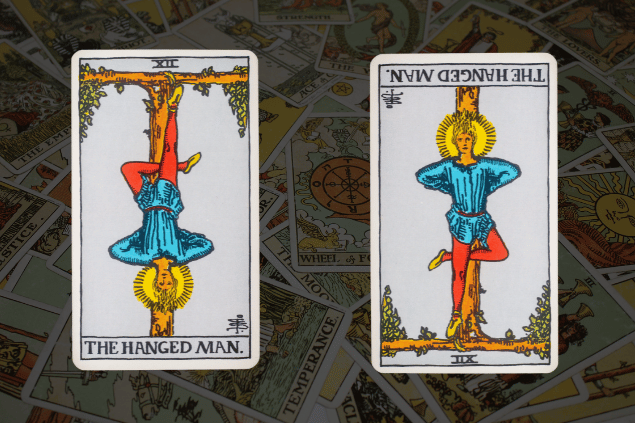 Montagem com a carta O Pendurado do Tarot na posição normal e outra carta O Pendurado na posição invertida. Ao fundo, há várias cartas de Tarot.