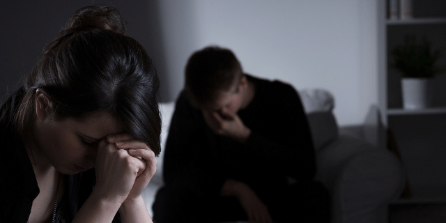 Duas pessoas sentadas de cabeça baixa tristes pela morte de alguém. 