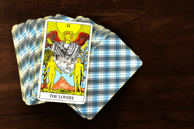 Na imagem, há a carta Os Enamorados sobre um baralho com cartas viradas para baixo. Embaixo, há uma mesa de madeira.
