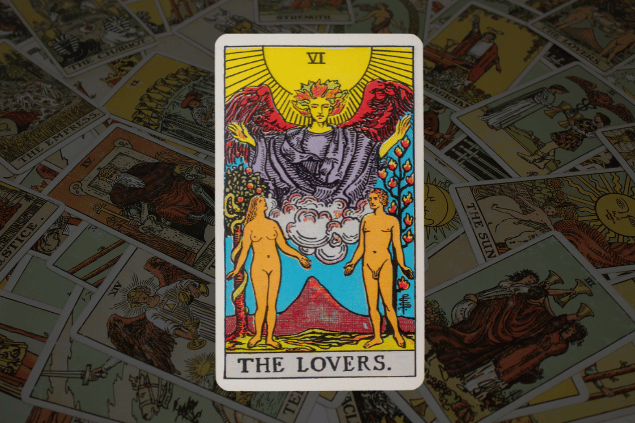 Montagem com a carta Os Enamorados do Tarot na posição normal. Ao fundo, há várias cartas de Tarot.