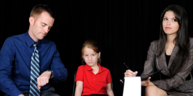 Menina sentada em uma cadeira entre um homem e uma mulher adultos.