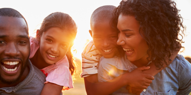 Um homem e uma mulher carregam crianças nas costas. Os quatro sorriem. 