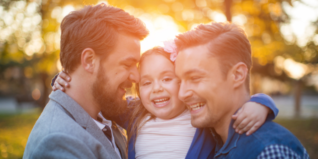 Dois homens carregam uma menina. Os três sorriem. 