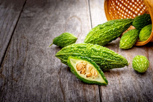 Melões de São Caetano sobre uma superfície de madeira, caídos de uma cesta tombada ao seu lado. Um dos melões está cortado ao meio, deixando as sementes à mostra.