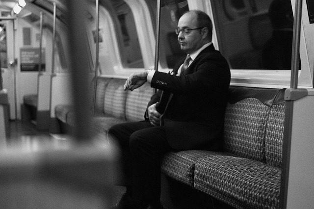 Homem branco engravatados sentada num metrô olhando para relógio de pulso.