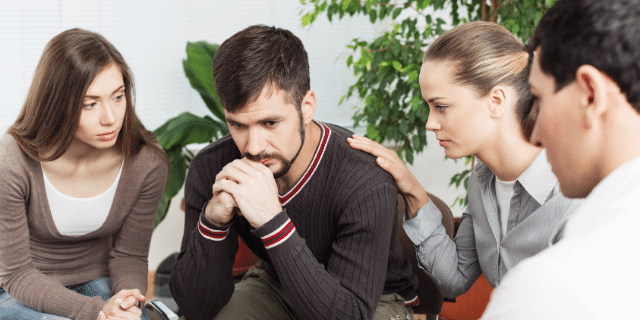 Um homem apreensivo com três pessoas em volta tentando acalmá-lo. 