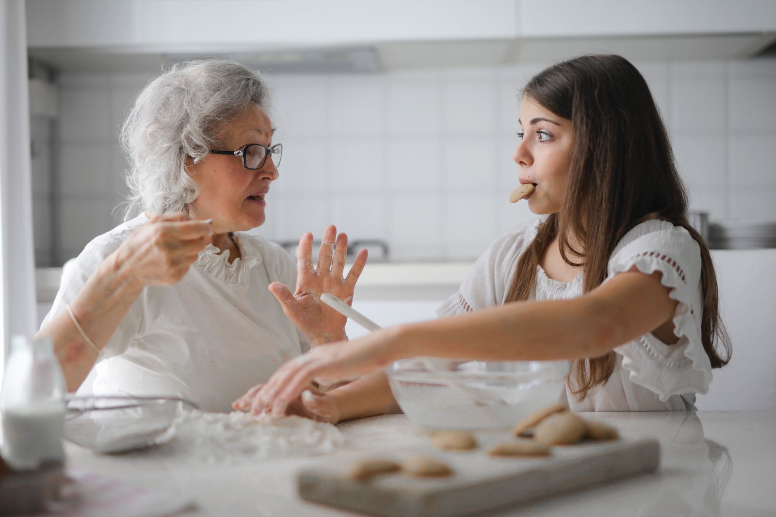 Foto de Andrea Piacquadio no Pexels Avó cozinhando com sua neta, que rouba um biscoito.