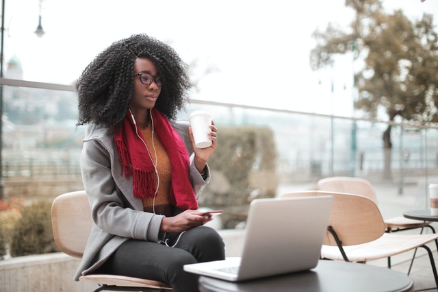Mulher negra sentada na sacada de um prédio, com notebook a sua frente.