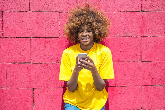 Mulher de cabelos cacheados sorrindo enquanto usa o celular.