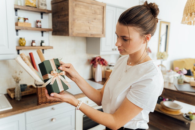 Mulher segurando um presente natalino com as duas mãos e olhando em direção a ele com um semblante não tão feliz
