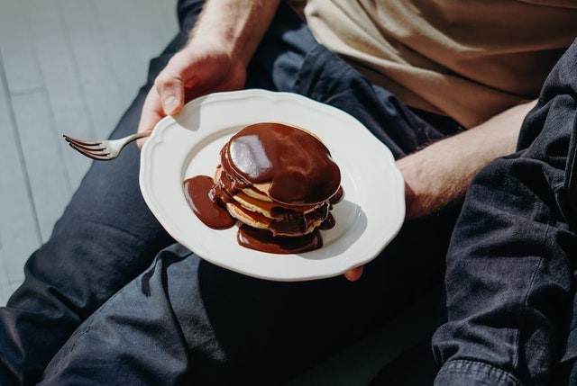 Homem segurando um prato com uma panqueca coberta de chocolate derretido