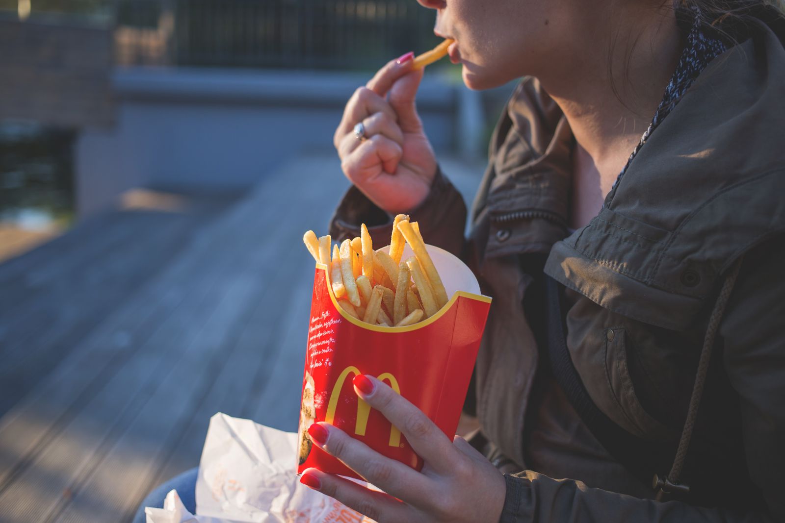 Mulher segurando batatas fritas do Mc Donalds e comendo