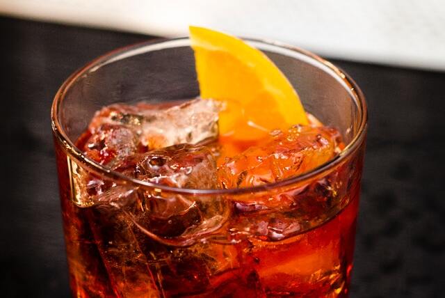 Copo com líquido marrom, cubos de gelo e fatia de limão.