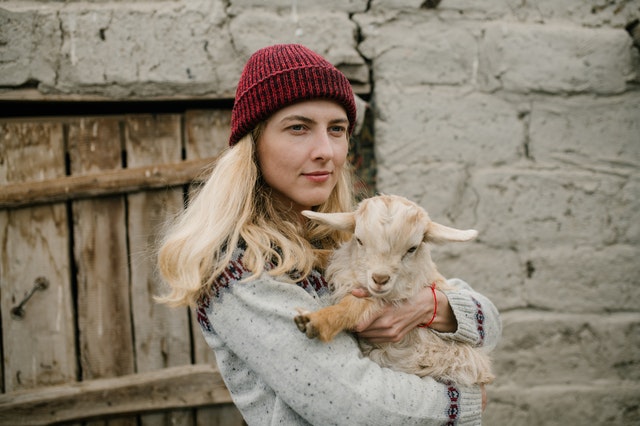 Mulher branca segurando bode no colo.