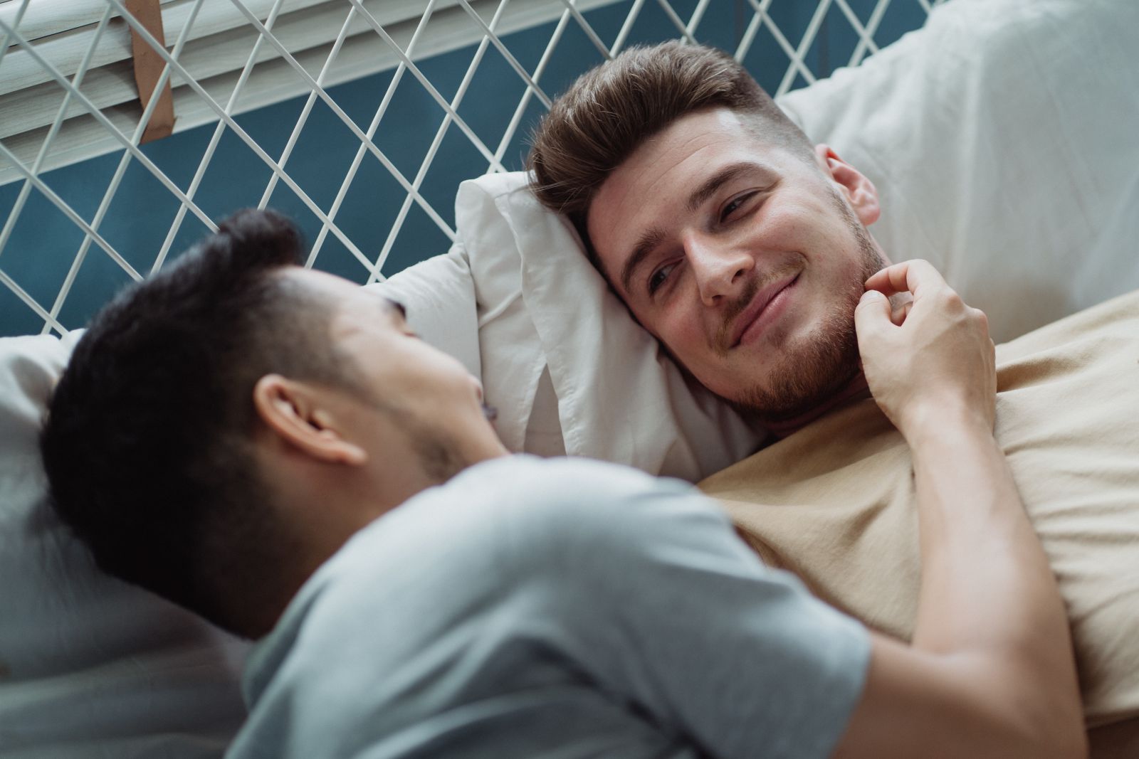Casal de homens deitados na cama sorrindo