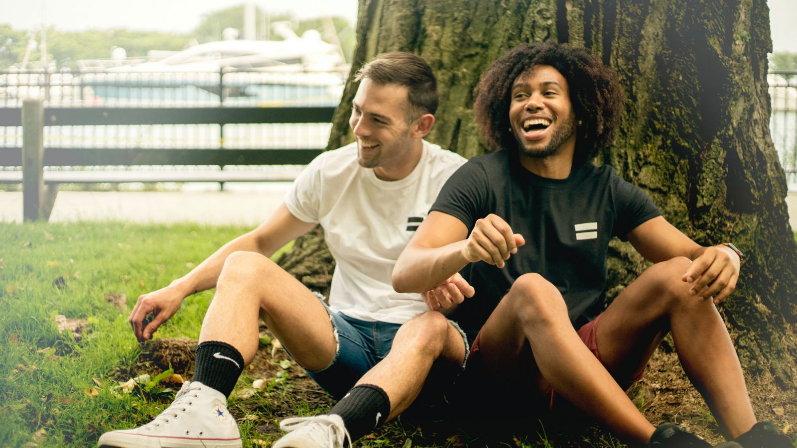 Dois homens sorrindo sentados ao lado de uma árvore