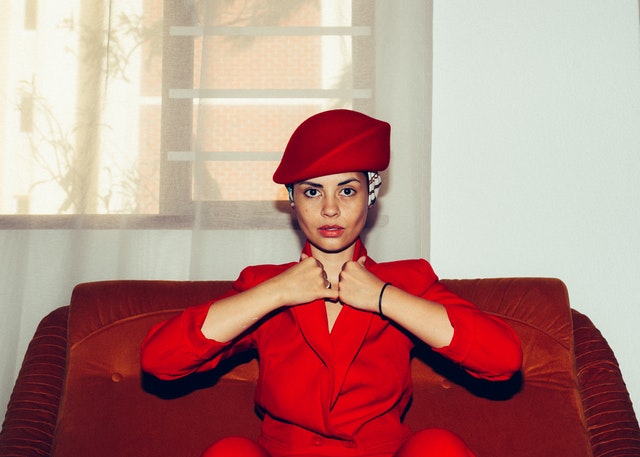 Mulher branca de roupas e chapéu vermelhos e mãos levadas ao colarinho.