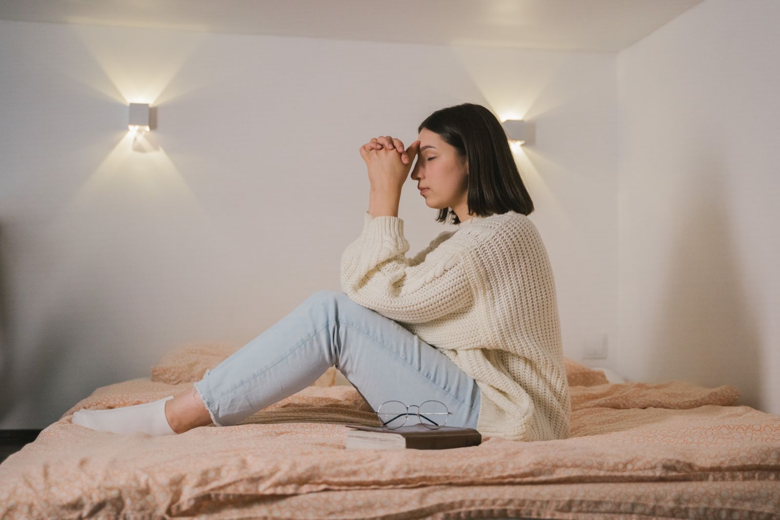 Mulher de olhos fechados sentada na cama orando 
