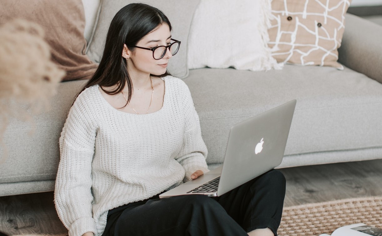 Mulher de óculos sentada no chão da sala mexendo no notebook