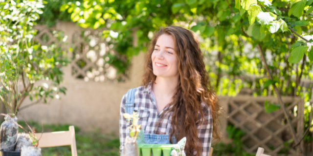 SrdjanPav / Canva Mulher pratica jardinagem em ambiente exterior. Ela sorri.