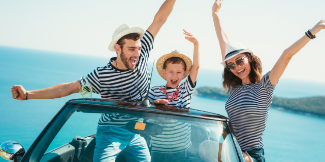 Família composta por três pessoas sorri dentro de um carro conversível. Há um homem, uma mulher e uma criança ao centro.