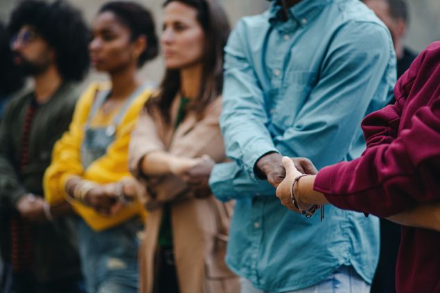 Pessoas segurando as mãos umas das outras, formando uma barreira com seus corpos.