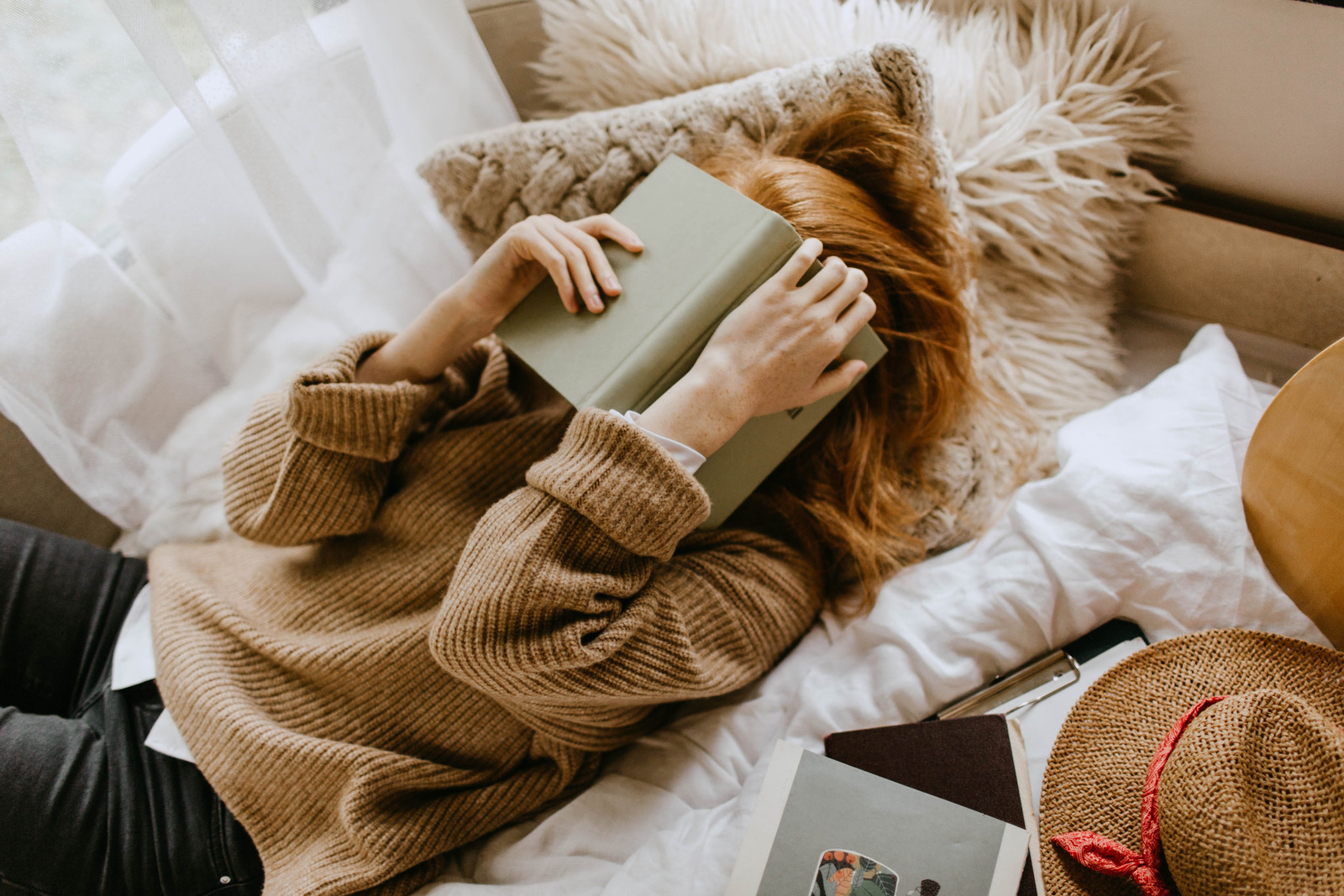 Mulher branca deitada numa cama com livro no rosto.