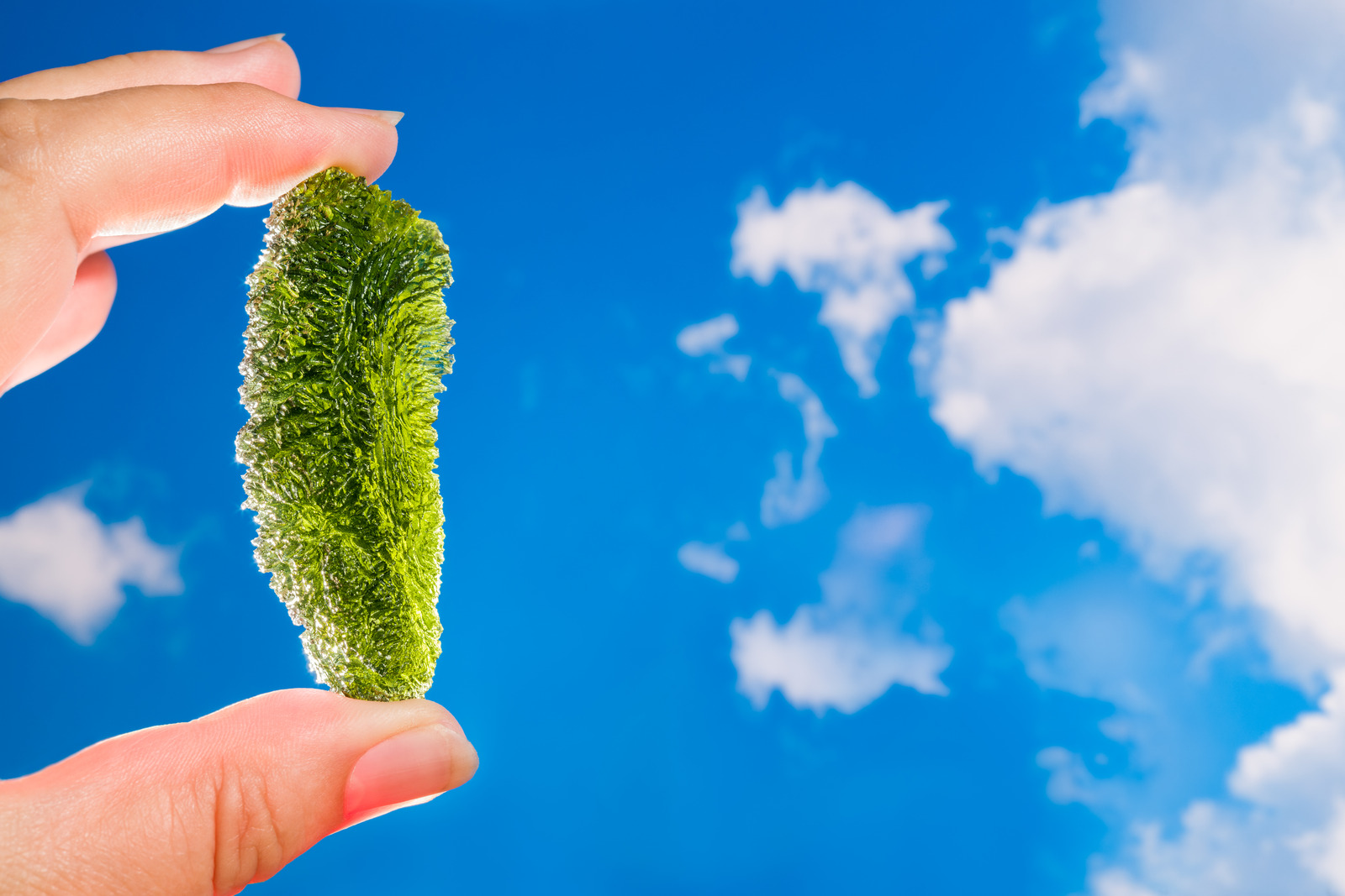 Pessoa segurando pedra verde num céu azul.