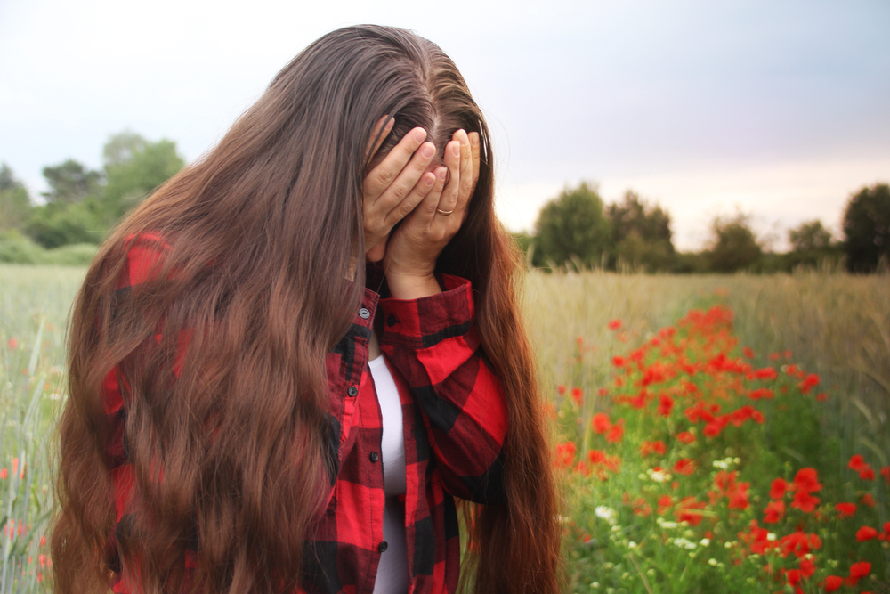 Mulher com as mãos no rosto, com vergonha