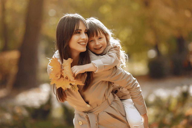 Mãe feliz carregando a filha pequena nas costas em um parque. 