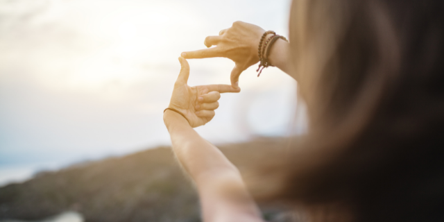 Mulher faz um quadrado com os dedos e observa por entre ele a paisagem. 
