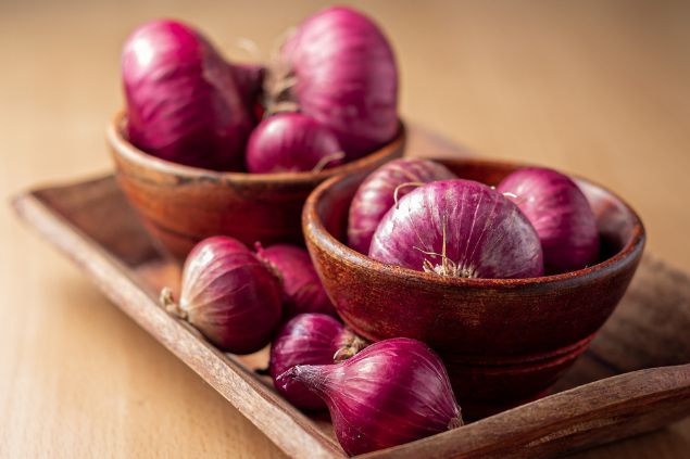 Várias cebolas roxas dentro de um recipiente sobre uma tábua.