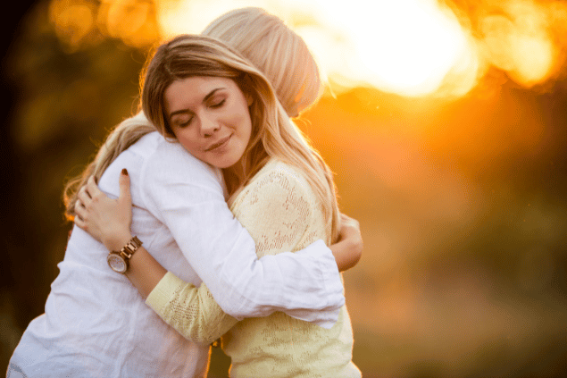 Mãe e filha se abraçando atrás de um por do sol iluminado