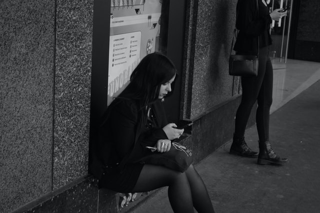 Mulher branca de cabelos curtos e pretos, sentada na rua.