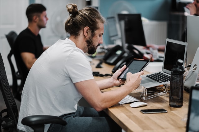 Homem branco segurando tablet numa sala de trabalho.