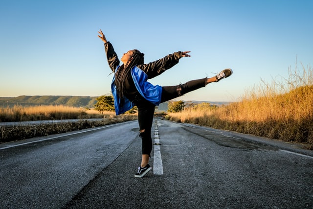 Mulher negra dançando numa estrada.