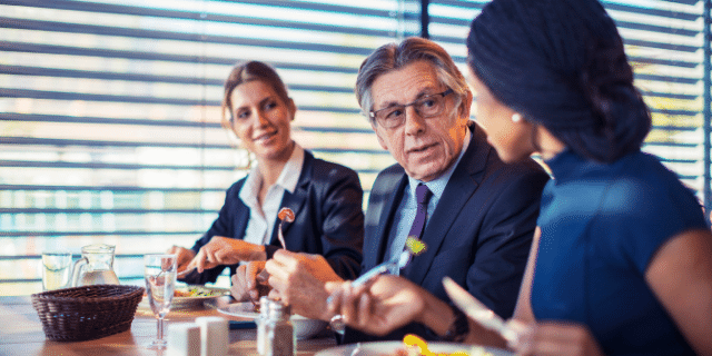 3 pessoas sentadas na mesa almoçando enquanto conversam. 
