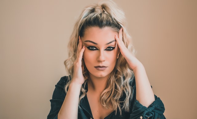 Mulher branca e loira com as mãos no rosto.