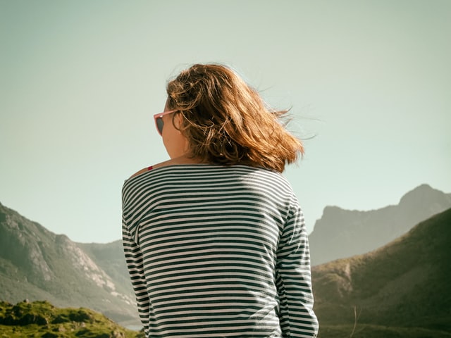 Mulher branca de costas numa paisagem.