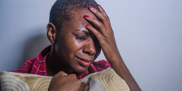 Mulher segura travesseiro e chora com a mão sobre a testa. 