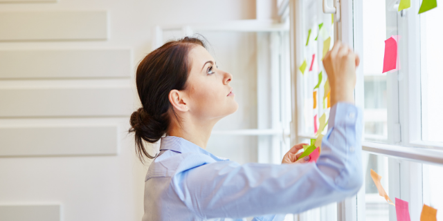 Mulher organiza post-its em parede. 